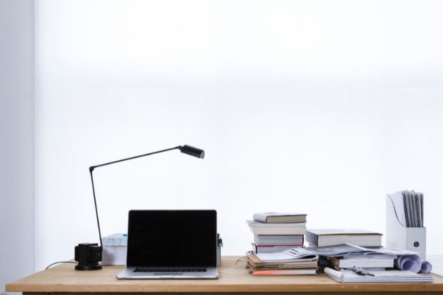 Un bureau en contre jour avec une lampe, des livres et des papiers.