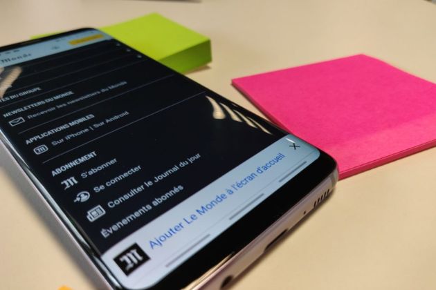 Téléphone portable avec l'application du Monde ouverte, à côté de deux blocs de Post-it.