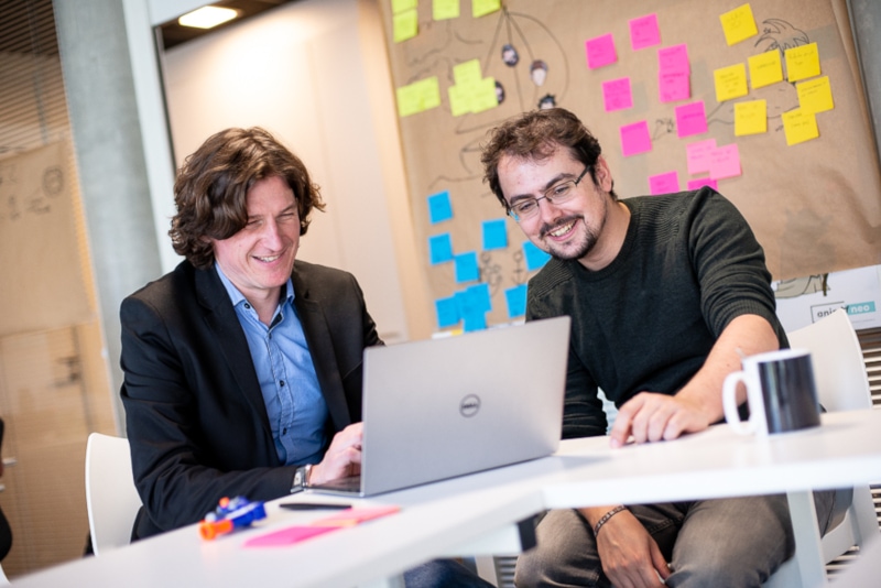 Hugo et Julien rient devant un ordinateur de l'agence Oniti.