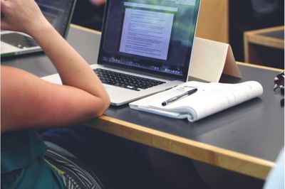 coude posé sur un bord de table devant un ordinateur ouvert