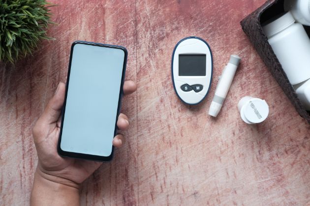 Vue en plongée d'une table montrant une main tenant un téléphone portable et des ustensiles médicaux utilisés dans le cadre du diabête.